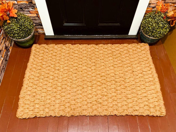 Beige doormat in front of a black door with decorative plants on either side.